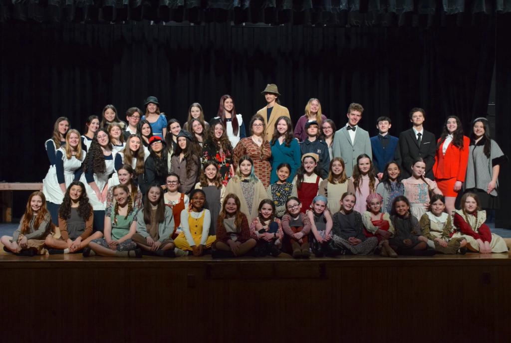 students sitting and standing on stage dressed in clothing for the play Annie